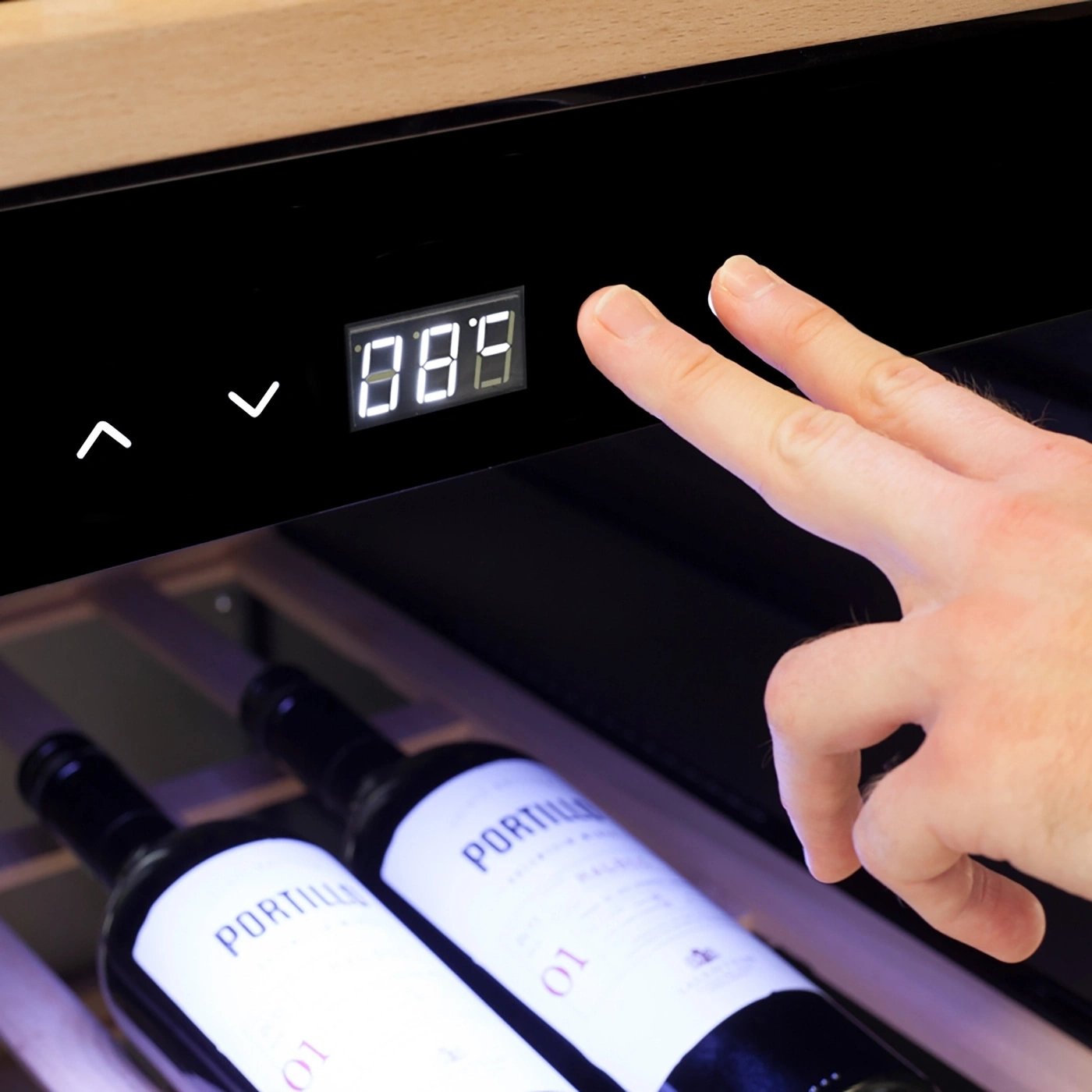Weinkühler mit Temperaturanzeige und Bedienung durch Finger, Weinflaschen im Hintergrund