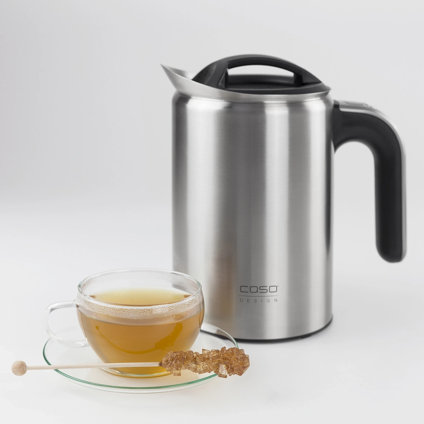 Teacup with tea and sugar stick next to a kettle with a handle