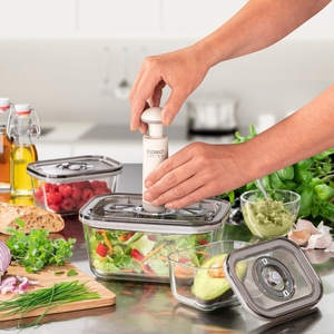 Person using a vacuum pump on food containers with vegetables and fruits.