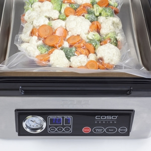 A vacuum sealer with a bag of vegetables being sealed.