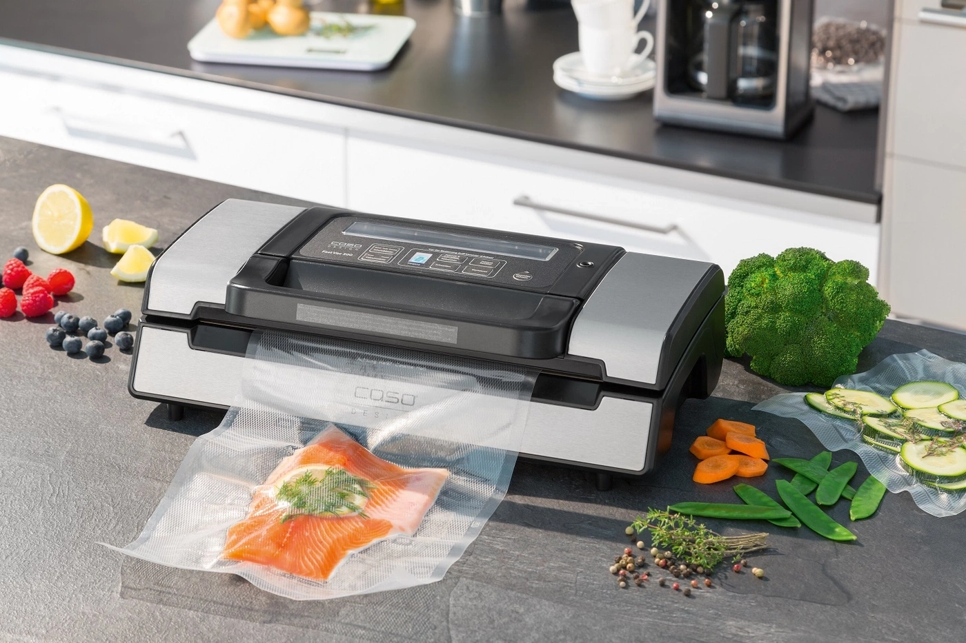 Ein Vakuumiergerät mit Lachs, Beeren und Gemüse auf einer Arbeitsplatte.